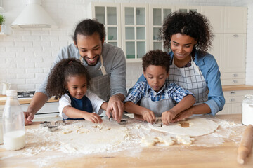 Happy African American parents with kids cooking homemade cookies in kitchen together, using cutters, loving young mother and father with little son and daughter spending leisure time at home