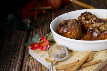 roasted red apples with cinnamon and honey in white earthenware dish on dark wooden table
