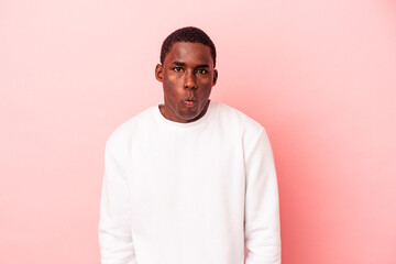 Young African American man isolated on pink background blows cheeks, has tired expression. Facial...