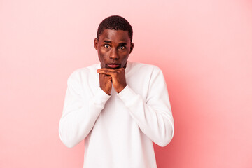 Young African American man isolated on pink background praying for luck, amazed and opening mouth looking to front.