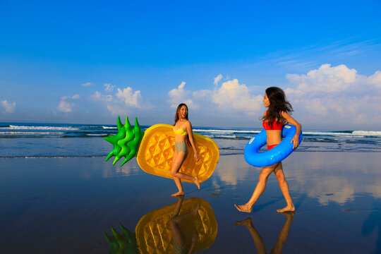 Smiling women holding swimming floats walking at beach