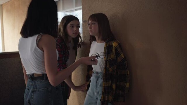 Nerd teenage girl standing at wall as bullies threatening pushing kid. Angry schoolgirls bullying smart cute teenager outdoors. Lifestyle and mistreatment concept