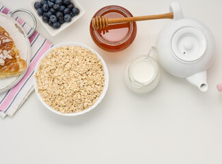Raw oatmeal in white ceramic plate, blueberry, honey on white table, breakfast. top view