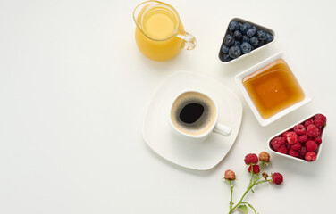 freshly squeezed juice in a glass transparent decanter, a cup of coffee, honey and oatmeal on a white table. Morning breakfast, top view