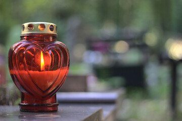 A red heart - shaped candle (snitch) on a tombstone in a cemetery during the day. All Saints' Day,...