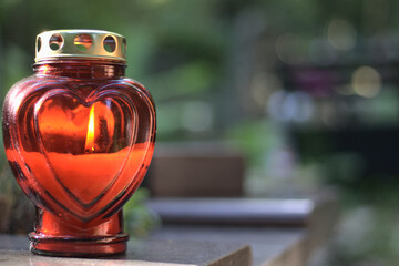 A red heart - shaped candle (snitch) on a tombstone in a cemetery during the day. All Saints' Day, copy space.