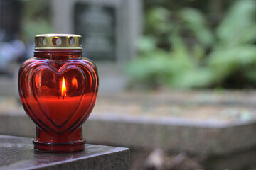 A red heart - shaped candle (snitch) on a tombstone in a cemetery during the day. All Saints' Day,...