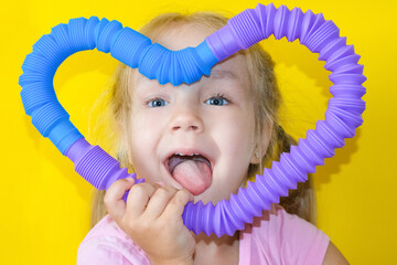 pop tube. anti stress sensory plastic toy from a pop tube in the hands of a child. Cheerful little girl playing with a toy fidget pop tube. trend of 2021. - obrazy, fototapety, plakaty