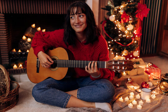 Young woman playing guitar while sitting at home during Christmas
