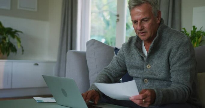 Animation of caucasian senior man doing paperwork and using laptop at home