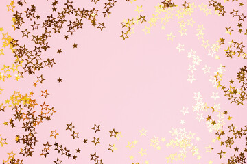 Border frame made of gold colored stars confetti on a pink pastel background.