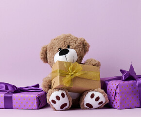 cute brown teddy bear and box wrapped in paper and silk ribbon on a purple background. Prize and...