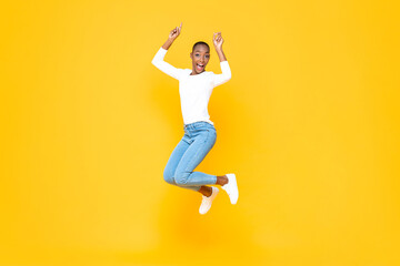 Fototapeta na wymiar Energetic young African American woman jumping with hands pointing up in isolated yellow studio background