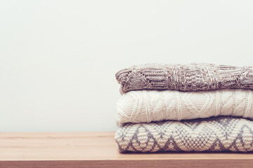 Obraz na płótnie Canvas Stack of knitted warm clothes on wooden background. Pile of sweaters on table. Autumn, winter season knitwear.