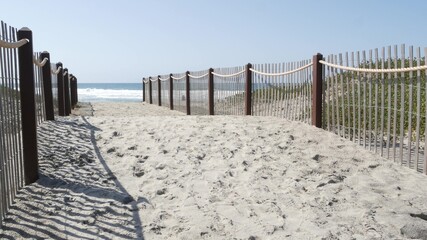 Pacific ocean coast, greenery and wooden picket fence on sea shore. Blue water waves on sunny...