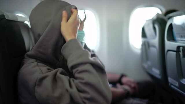 Young woman sitting next to a man on board the airplane and wearing a face mask, preparing to take a nap during flight