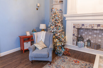 Classic Christmas decorated interior room, New year tree with silver decorations. Modern blue classical style interior design apartment with fireplace and armchair. Christmas eve at home.