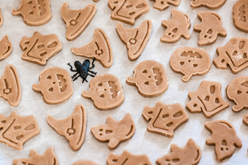 Preparing to celebrate halloween and preparing a treat. Raw ready-to-bake halloween cookies on paper on a baking sheet. Lifestyle