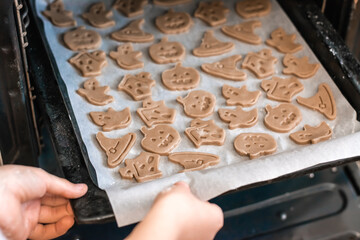 Preparing to celebrate halloween and preparing a treat. Hands insert a baking sheet of raw Halloween cookies into the oven. Lifestyle