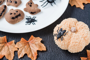 Decorating the table with needlework for Halloween. Black fly on a knitted pumpkin against the background of gingerbread cookies on a plate. Traditional celebration