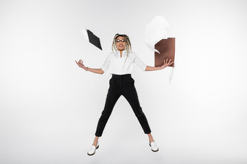 joyful african american businesswoman levitating near folders and documents isolated on white