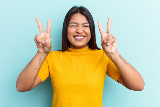 Young Venezuelan woman isolated on blue background showing victory sign and smiling broadly.