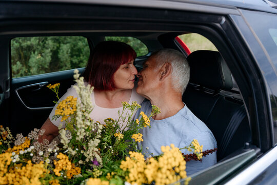 Romantic senior couple sitting with tansy flowers while kissing in car