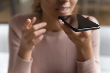 Crop close up of young Caucasian woman hold modern smartphone record audio message or talk on loudspeaker on gadget. Female speak activate digital virtual voice assistant on cellphone device.