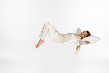 young african american woman sleeping in silk pajamas while levitating isolated on white