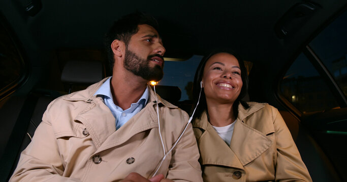 Young couple sharing earphones resting in backseat of car
