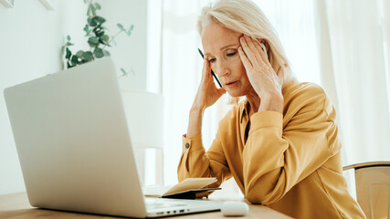 Handsome mid aged woman at her bright and sunny apartment. Tired of computer with headache