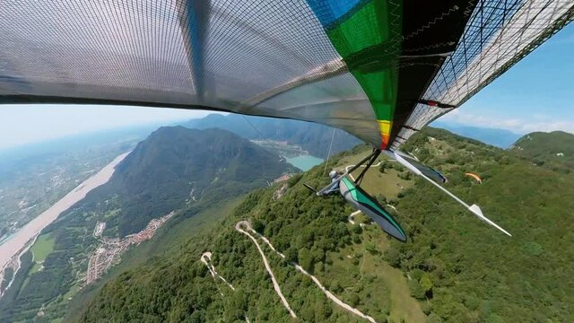 Hang glider soars in the mountain valley above serpentine road in Bordano, Italy