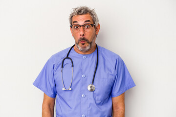 Middle age nurse caucasian man isolated on white background  shrugs shoulders and open eyes confused.