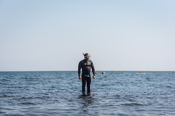 Diver in the wetsuit is standing on the sea background. Snorkeling.