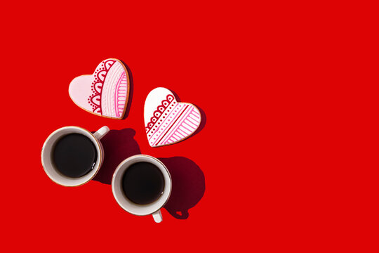 Studio shot of heart shaped cookies and two cups of coffee standing against red background