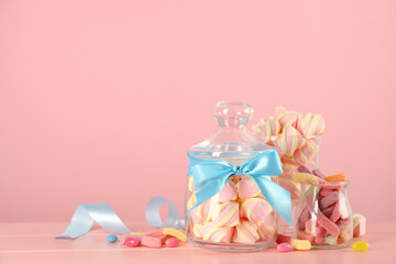 Jars with different delicious candies on pink wooden table, space for text