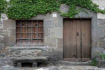 Facade of an old stone house with a wooden door and window, in front it has a stone bench and a...