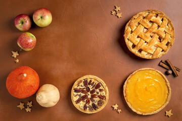 Three homemade autumn pies on brown background. Traditional American desserts. Pies with pumpkin, apple and pecan for Thanksgiving day. Top view, copy space.