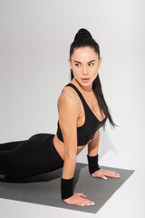 Fototapeta premium young woman in black sportswear exercising on fitness mat on grey