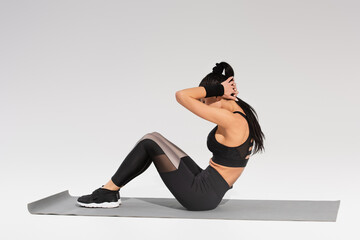 full length of woman in black sportswear doing do ups on fitness mat on grey
