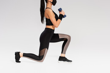 cropped view of sportswoman in black protective mask exercising with dumbbells on grey