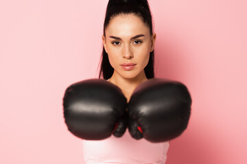 young strong woman in sportswear and blurred boxing gloves on pink