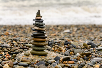 Fototapeta na wymiar Pyramid of pebbles on the beach.Waves in background