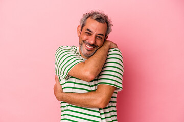 Middle age caucasian man isolated on pink background  hugs, smiling carefree and happy.