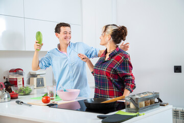 pareja joven jugando en la cocina mientras cocinan verduras en una cocina blanca, bol rosa, sarten...