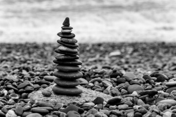 Pyramid of pebbles on the beach.Waves in background, black and white