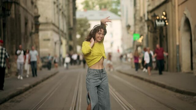 Outdoor summer lifestyle video of young pretty hipster woman having fun, listening music and dancing on the street, city center Europe, fun ,joy, emotions