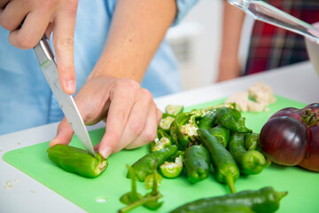 chico joven cortando pimientos verdes en una tabla de cortar verde con tomate sobre una encimera blanca