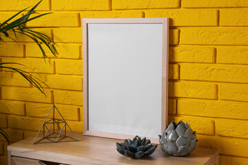 Empty frame and decor on wooden cabinet near yellow brick wall. Mockup for design