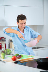 hombre joven sonriente batiendo huevos en bol rosa con camisa azul, men at work en cocina blanca